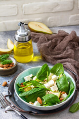 Couscous salad with pear, spinach, almonds, feta cheese and vinaigrette sauce on a gray stone table. Copy space.