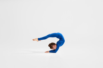flexible child girl in blue sportswear performs gymnastic exercises on studio background