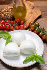 Cheese collection, white balls of soft Italian cheese mozzarella, served with red cherry tomatoes, fresh basil leaves