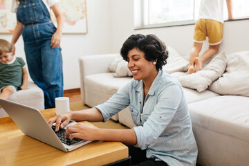 Woman working on laptop with her family in background