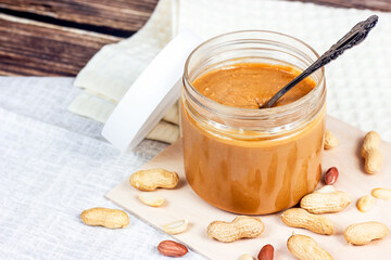 Fresh homemade crunchy peanut butter with nuts on light wooden background in the kitchen.