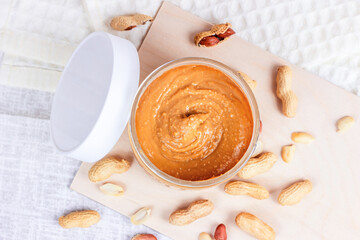 Top view of fresh homemade crunchy peanut butter with nuts on light wooden background in the kitchen.