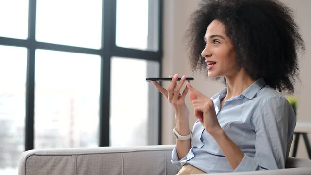 Young biracial businesswoman with afro hairstyle wearing formal shirt holding a mobile phone and recording a voice message, a female entrepreneur talking, chatting, using voice recognition app