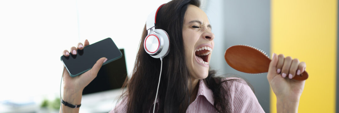 Woman with headphones and comb in her hands sings emotionally. Stress relief while singing concept
