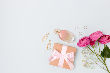 Layout of flowers bouquet, gift with tied bow, feminine accessories on a blue background. Tenderness female composition with copyspace.