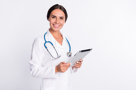 Photo of adorable positive young woman doctor wear formal coat holding modern gadget empty space isolated white color background
