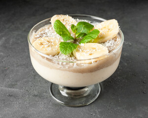 milk pudding with banana layer and decoration of coconut, mint and fresh banana on gray concrete background