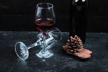 Glasses of red wine with bottle and pinecone on stone table