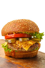 Classic burger with beef, cheese vegetables in sauce on a bun with sesame seeds on a brown wooden board on a white plate.