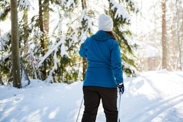 Fototapeta na wymiar Winter sport in Finland - cross-country skiing. Pregnant woman skiing in sunny winter forest covered with snow. Active people outdoors. Scenic peaceful Finnish landscape.