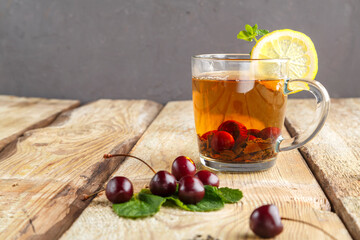 black tea in a glass cup with mint cherries and lemon on a wooden table near fresh cherries.