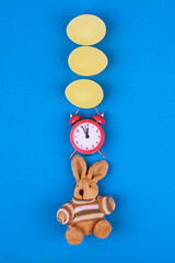 Easter concept with alarm clock, bunny toy and eggs on light blue background.