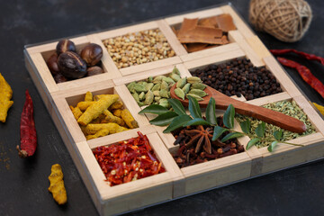 Indian spices for Indian cooking Masala hot spicy curry  whole spices turmeric, cardamom, black pepper in wooden spoon curry leaves paprika in Indian spice box Kerala India Sri Lanka.