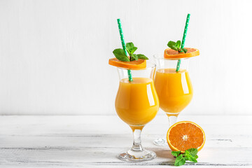 Fresh orange juice cocktail in a glass with a straw decorated with mint leaves on a white wooden table. Selective focus.