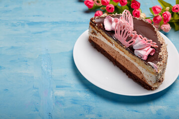Half of cake on white plate on blue painted background. Sweet bakery with artificial spring flowers