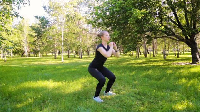 
 Young attractive woman dressed in sports uniform doing squats. Sports activities in the park. Healthy lifestyle concept.