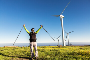 Satisfied hiker celebrating success in meadow with windmills