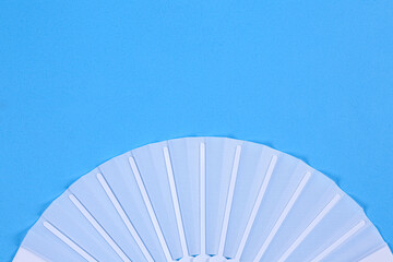 White hand fan on light blue background, top view. Space for text