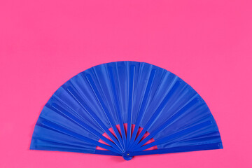 Blue hand fan on pink background, top view