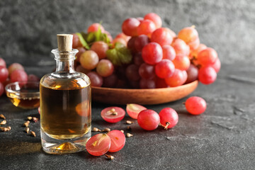 Organic red grapes, seeds and bottle of natural essential oil on black table. Space for text.