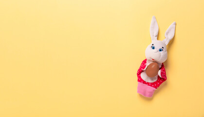 Banner with Easter bunny keeping the chocolate egg on yellow background with copy space, empty text place. Christian holiday card. Online course learning of toy theater. Painting eggs. Hand puppet