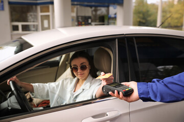Woman sitting in car and paying with credit card at gas station, focus on hand