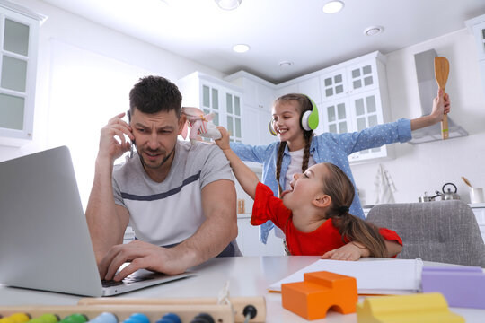 Children Disturbing Stressed Man In Kitchen. Working From Home During Quarantine