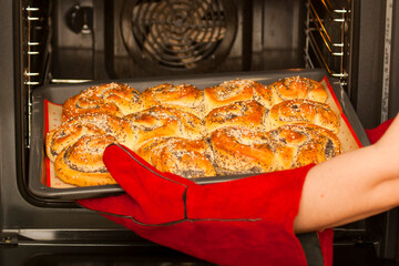 Fresh baked goods from the oven. A baker wearing heat-resistant gloves takes out baked goods from the electric oven