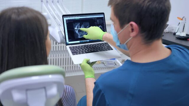 Dentistry doctor talking about surgery showing x-ray on monitor to patient