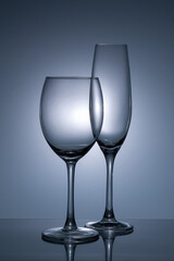 Two wine glasses of smooth white glass on a gray-blue background. Monochrome. Wine glass and champagne glass. Still life.