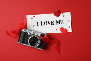 Paper with handwritten phrase I Love Me, camera and hearts on red background, flat lay