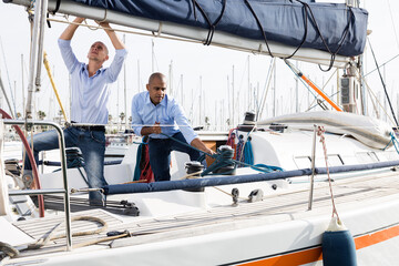 Two men in blue shirts and jeans working on sailing yacht in the port