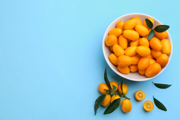 Fresh ripe kumquats with green leaves on light blue background, flat lay. Space for text