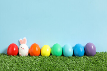 Bright Easter eggs with bunny ears on green grass against light blue background