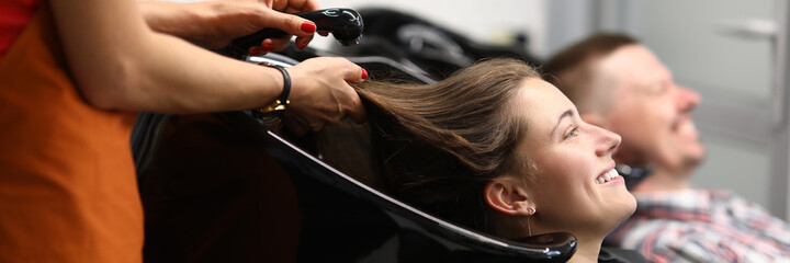 Happy visitor to beauty salon lie with her head in black washbasin and wait for hairdresser to wash...