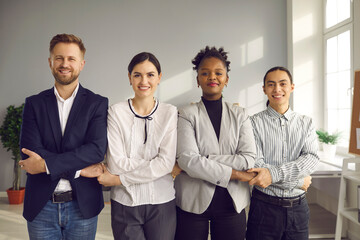 Four happy smiling young multiracial people who work in one and same company standing in row, holding hands and looking at camera. Business team, community support, strength, corporate success concept