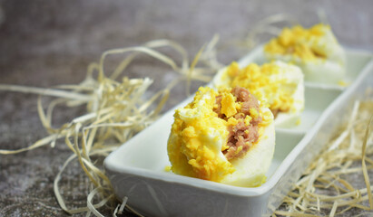 Eggs stuffed with tuna, mayonnaise layer and grated yolk. Presentation in a rectangular plate on a stone background.
