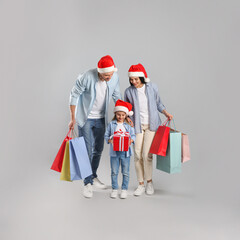 Happy family with paper bags and gift on grey background. Christmas shopping
