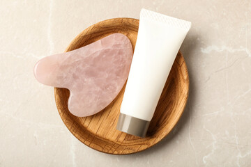 Rose quartz gua sha tool and cosmetic product on grey table, top view