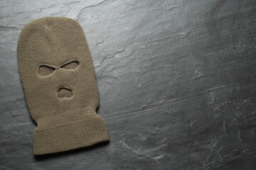 Beige knitted balaclava on black table, top view. Space for text