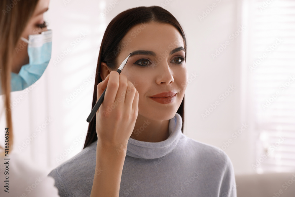 Wall mural Makeup artist in protective mask working with woman indoors. Preventive measures during COVID-19 pandemic