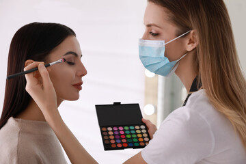 Makeup artist in protective mask working with woman indoors. Preventive measures during COVID-19...