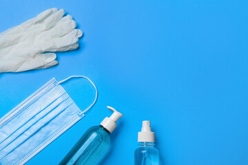 Medical gloves, mask and hand sanitizers on light blue background, flat lay. Space for text