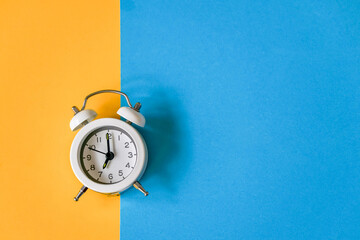 white vintage alarm clock on two tone color grunge paper , yellow and blue background , time...