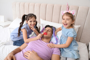 Cute little children painting face of their father while he sleeping in bed at home