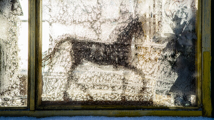 Silhouette of horse toy on sill behind window. Frost patterns on glass