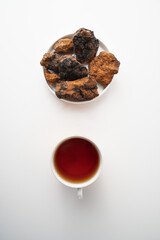 Chaga, birch tree mushroom in white plate and chaga tea on grey background. Natural medicine, antioxidant, superfood. Vertical.