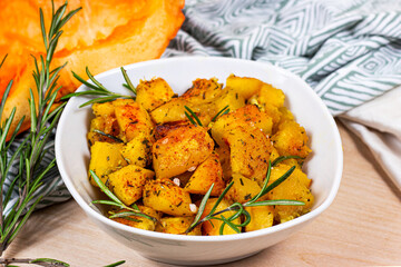 Fresh baked pumpkin pieces with rosemary and spices in white bowl on light background.