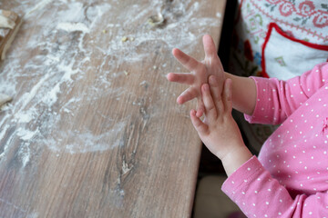 Hands of little caucasian kid trying to cook or play with flour at the table at kitchen, cooking family concept, copy space.