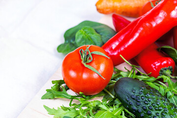 Fresh farm summer vegetables for salad: cucumbers, tomatoes, onions, arugula leaves in the kitchen on light background.